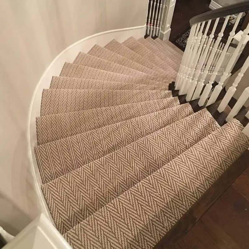 A curved staircase with herringbone carpet runner and white spindles